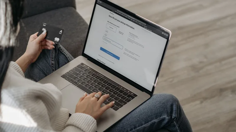 A shopper holds a credit card while checking out on a laptop, the moment to pause and verify before paying