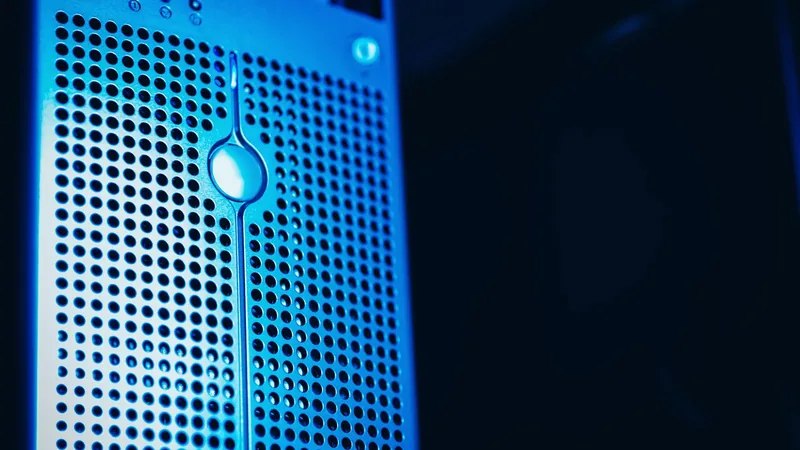 The perforated front panel of a rack-mounted server lit blue in a dark data centre, a single power indicator glowing near the top.